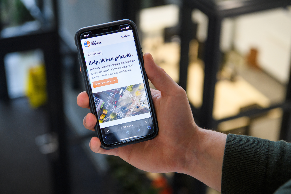 Foto van een hand met een mobiele telefoon waarop de website HackHelpdesk is te zien