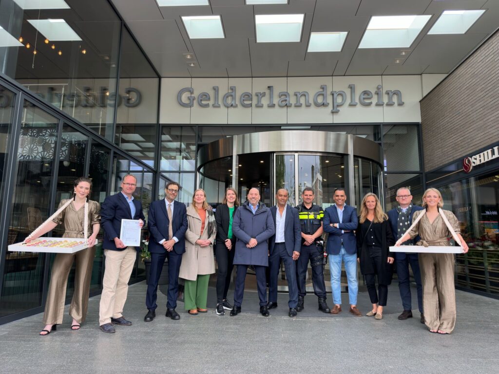 Foto uitreiking KIWA certificaat voor de ingang van winkelcentrum Gelderlanplein met betrokkenen.